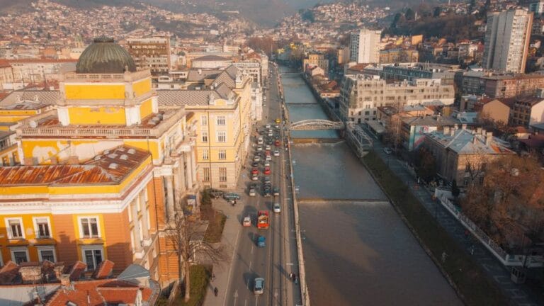 City trip aux Balkans sans voiture : guide transports 2026 Aerial view of Sarajevo with Miljacka River, showcasing urban architecture and mountain backdrop.
