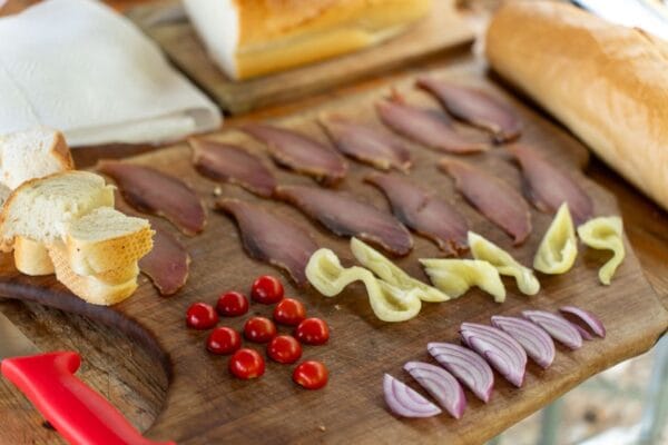 Gastronomie des Balkans : plats typiques et spécialités locales Delicious charcuterie board featuring sliced meat, bread, tomatoes, onions, and peppers on a wooden board.