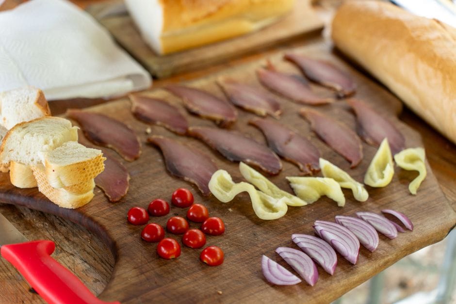 Gastronomie des Balkans : plats typiques et spécialités locales Delicious charcuterie board featuring sliced meat, bread, tomatoes, onions, and peppers on a wooden board.
