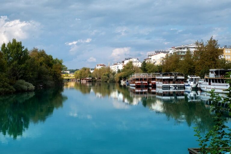 Bosnie-Herzégovine : que voir, faire et goûter en voyage ? Peaceful riverside view with moored boats, lush greenery, and overcast sky in a serene town setting.