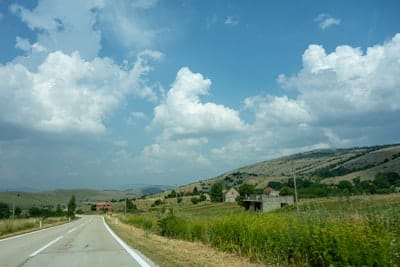 gray asphalt road between green grass field under blue and white cloudy sky during daytime
