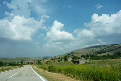 gray asphalt road between green grass field under blue and white cloudy sky during daytime